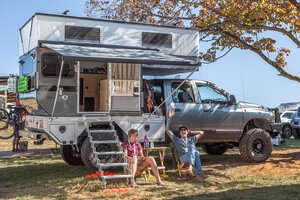Photo of two people lounging in front of a truck camper at Overland Expo East 2019.