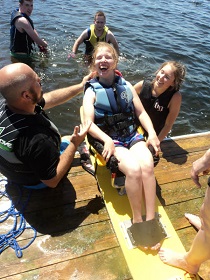 A photo of a physically challenged girl participating in watersports. Two people are helping the girl, and two other people are in the water behind them.