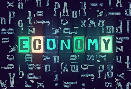 A picture of different green tile letters spelling out the word "economy" with other letters scattered on a black surface behind.