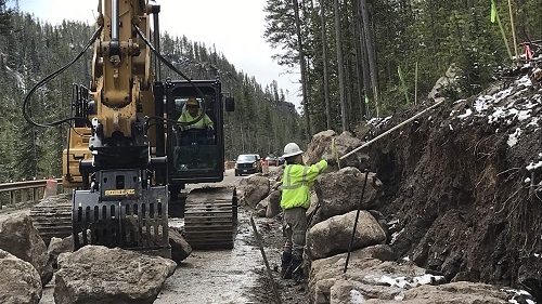 A picture of construction workers doing road work using a backhoe after a mud and rock slide.
