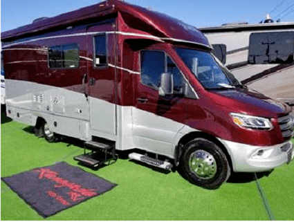A photograph of a Renegade RV 2020 Villagio with a welcome mat at the bottomo of its stairs sitting on astroturf.