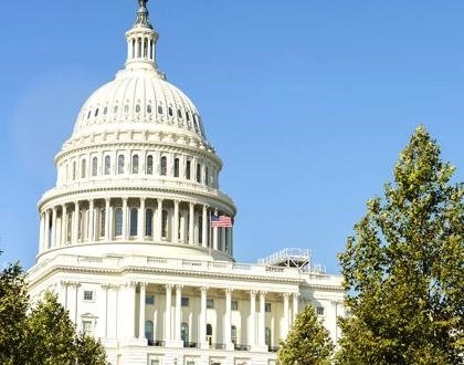 A picture of part of the U.S. Capitol Building in front of a clear blue sky. The American flag is flapping in the wind.