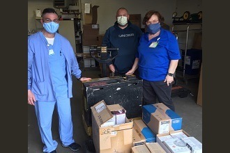 A picture of three people wearing medical masks standing next to several boxes of donated medical supplies