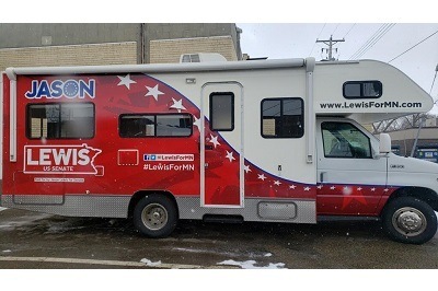 A picture of a Type C RV that is painted to look like a red banner with white stars is swooping down the side. The words "Jason Lewis U.S. Senate" and "www.LewisForMN.com" appear on the RV as well.