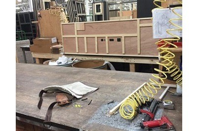 A picture of a work bench inside of a manufacturing warehouse. There are tools and cords across the bench.