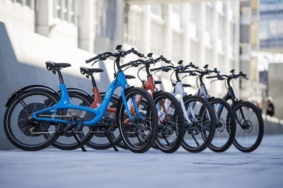 Five Elby electric bikes of different colors are arranged side-by-side in a row