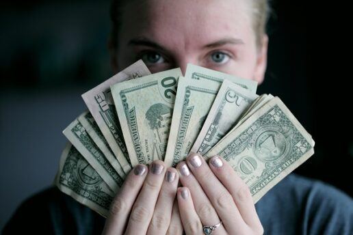 A photograph of a woman holding bills in varying monetary denominations fanned out in front of her face.