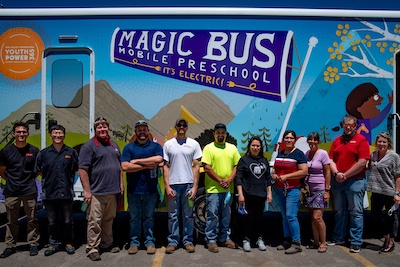 A photo of teachers in front of the Magic Bus Mobile Preschool.
