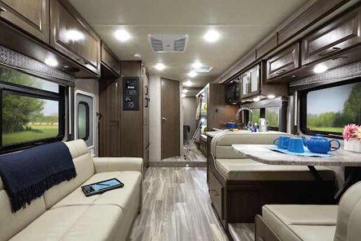 A picture of the interior of Thor Motor Coach's 2021 Fourwinds 31E. The picture shows a sofa on the left and a dinette on the right. Cabinetry above the furniture is a grayish brown.