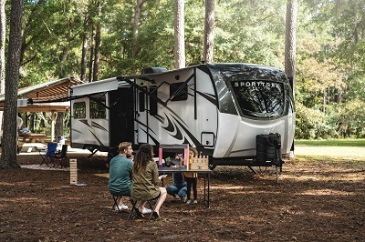 A picture of the Venture RV Sporttrek Touring RV in a campground with family in front of it
