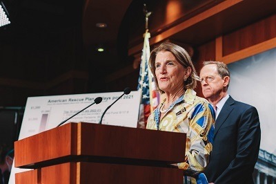 A picture of West Virginia senator Shelly Moore Capito at a podium announcing an infrastructure bill counter offer. Senator Pat Toomey is standing behind her in the background.
