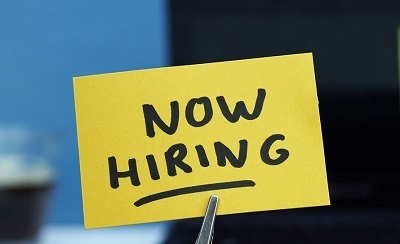 A picture of Now Hiring written on a sticky note, held by tweezers