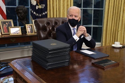 A picture of President Joe Biden with a stack of executive orders