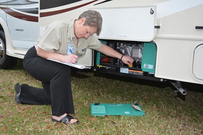 A picture of NRVIA inspector Sue Pendarvis kneeling on the ground as she examines the generator of an RV.