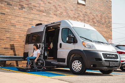A picture of the 2022 Winnebago Roam accessibility enhanced Type B van with a woman in a wheelchair on the wheelchair lift