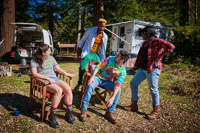 A picture of four friends camping outdoors, two of whom are sitting and white and two of whom are standing and Black