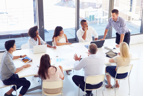A picture of a man leading a discussion with a small group of people around a conference table