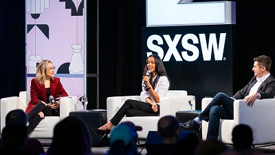 A picture of three panelists sitting in white chairs on a stage at the 2019 South by Southwest conference in Austin, Texas
