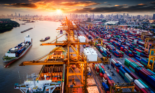 A picture of a shipping dock with various colored containers waiting to load onto a large boat