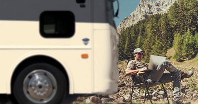 A picture of a person sitting in a camping chair outside their RV working on a computer with a large mountain in the background