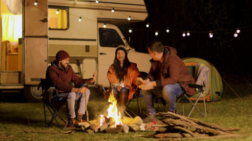 A picture of three people sitting around a fire outside a Type C RV in the dark.