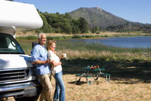 A picture of an elderly couple leaning against an RV at the shore of an alpine lake.