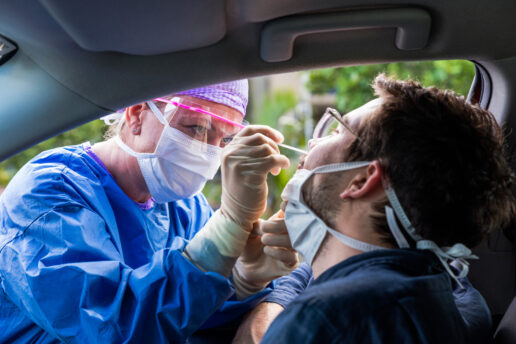 A nurse is seen leaning into a car window to administer a COVID-19 test.