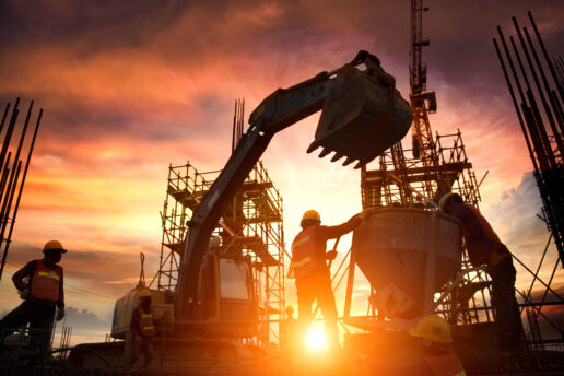 A picture of a silhouette of a team of contractors and a front-end loader on a construction site with a sunrise framing the group.