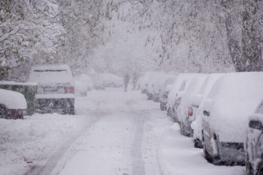 A snow-covered street with cars parked on the side of the road.