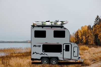 A picture of the Encore RV ROG 15PH travel trailer outdoors near a lake with fall trees in the background