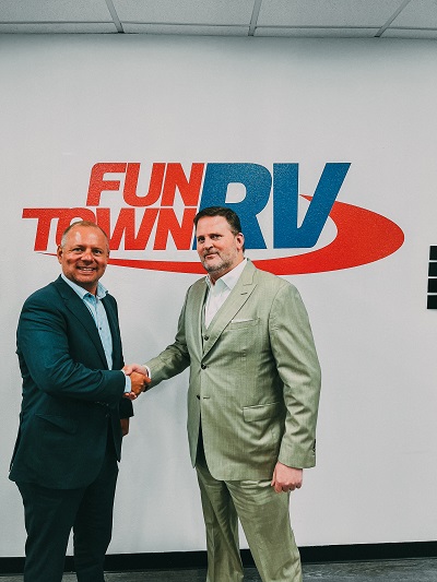 A picture of new Fun Town RV Vice President TJ Smith shaking hands with CEO Jarrod McGhee in front of a wall with a Fun Town RV logo