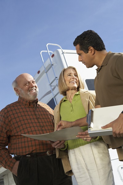 A stock image of an RV salesman completing a sale with an older couple in front of an RV on the lot