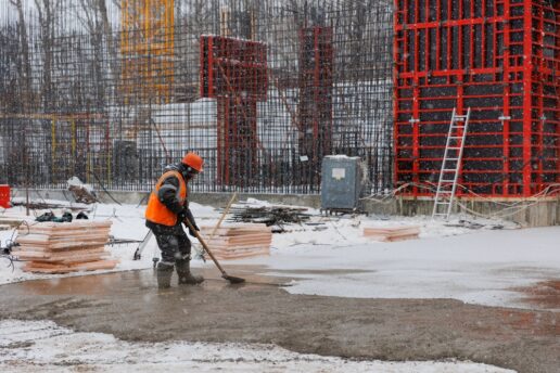A stock image of a man shoveling snow outside a building under construction