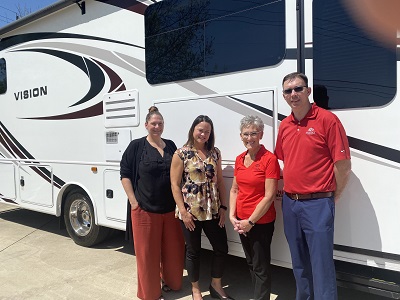A picture of three women and one man in front of a motorhome with the word "vision" printed on it.