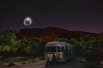 A picture of an RV at night with an eclipse of the moon in the background
