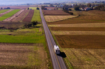 A picture of an asset from the RVIA Go RVing portal showing an RV on the open road through farmland