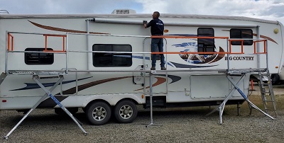 A picture of a worker on the Scissor Deck 16-foot platform system, working on the awning of an RV