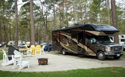 A picture of a Type C motorhome parked at a camping spot under the trees at a KOA campground.