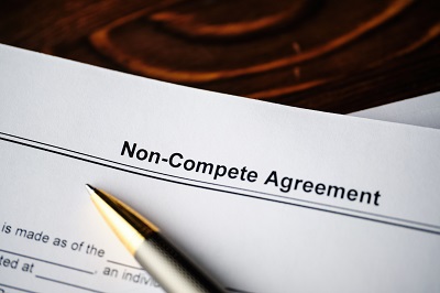 A picture of a legal document with the title Non-Compete Agreement at the top and a pen laid across the paper.