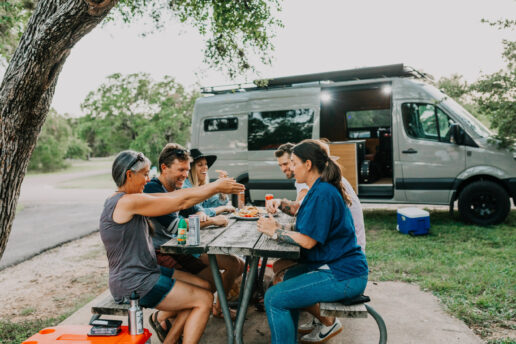 A stock picture of six adults sitting at a picnic table outside their Type B motorhome