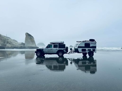 A picture of a Jeep pulling a Sunset Park RV towable on a beach.