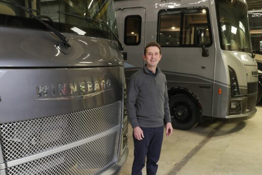 A picture of Winnebago-brand President Huw Bower standing in front of a row of Type A motorhomes at the company's Forest City, Iowa, plant.