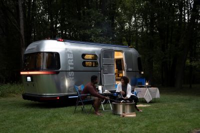 A picture of a couple outside roasting marshmallows in front of an Airstream eStream motorhome