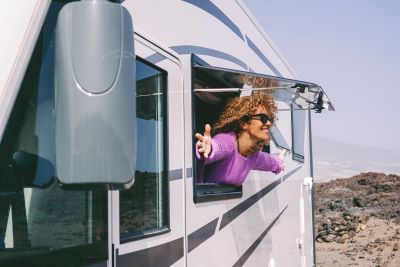 A picture of a curly-haired woman leaning out an RV window with her arms spread wide