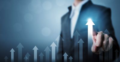 A picture of a stock image of a man in a suit in front of a chart graphic with up arrows depicting growth
