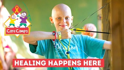 A picture of Care Camps marketing featuring a bald child holding a bow and arrow with the message Healing Happens Here below