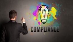 A picture of a man in a suit writingon a chalkboard with the word "Compliance" next to him on the board and a colorful lightbulb image