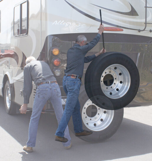 A picture of the 195250-S spare tire carrier carrying a spare tire with two men using the carrier outside the motorhome