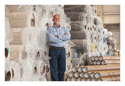 A picture of Rudy in front of Dicor PVC rolls in a warehouse