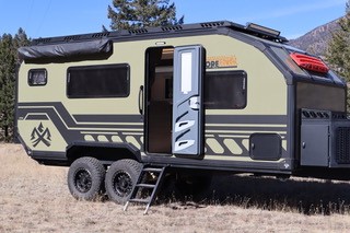 A picture of the Xplore X195 off_road travel trailer outside with its door open under a blue sky